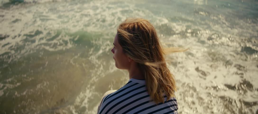 Cinemagraph of a thoughtful woman watching the sparkling ocean waves as the wind blows through her hair