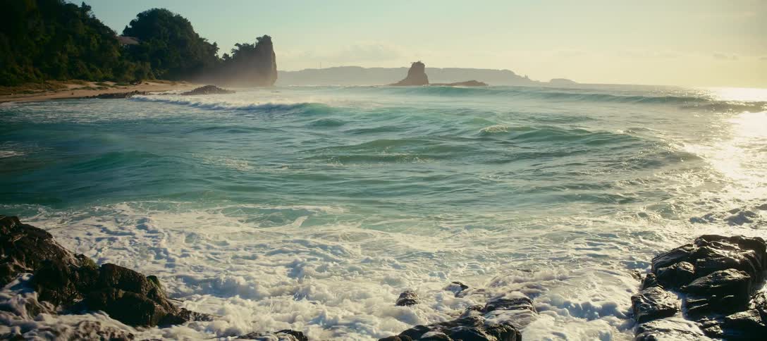 Slow motion view of powerful turquoise ocean waves crashing on a rocky tropical shoreline at sunrise