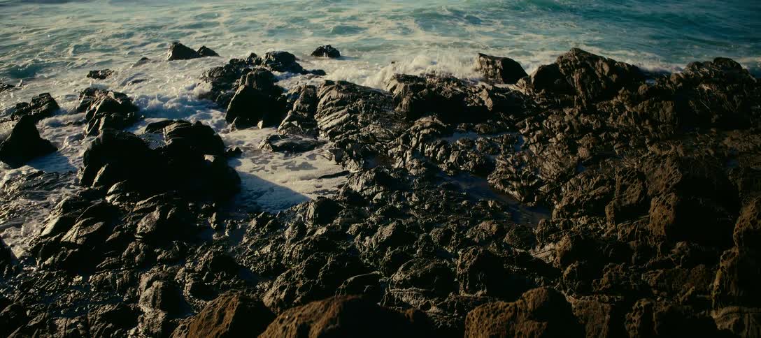 Slow motion shot of ocean waves crashing against a rocky shore in the warm morning light