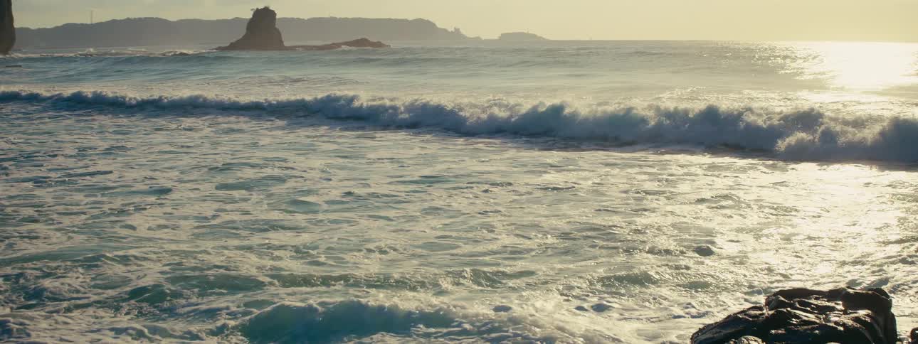 Mesmerizing slow-motion footage of ocean waves crashing and creating white foam against the shoreline during a golden sunset