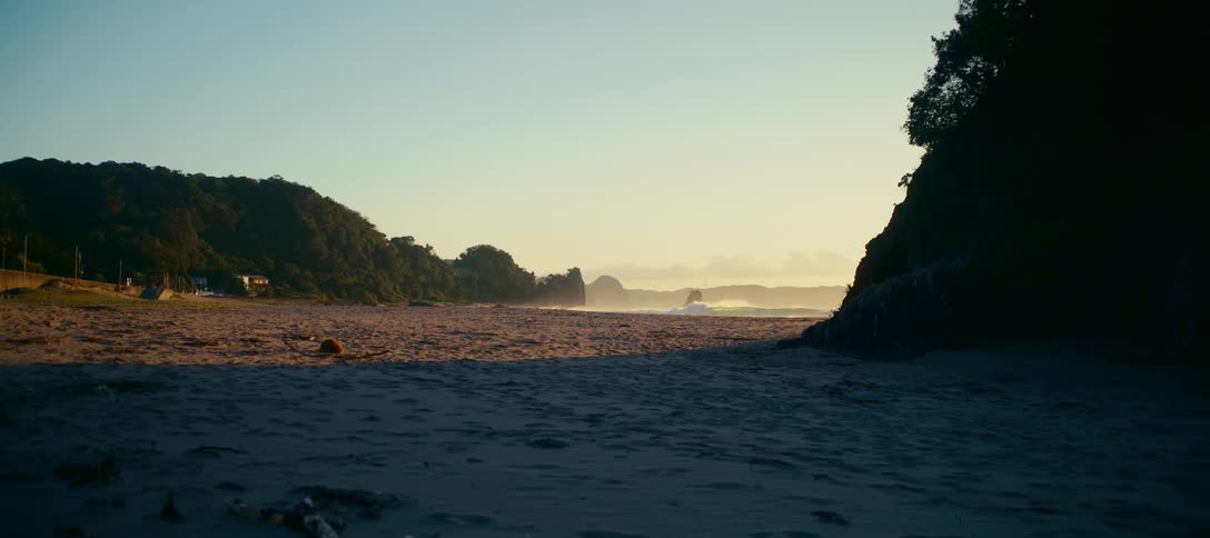 Golden morning light illuminates a tranquil, sandy beach cove as gentle ocean waves roll in