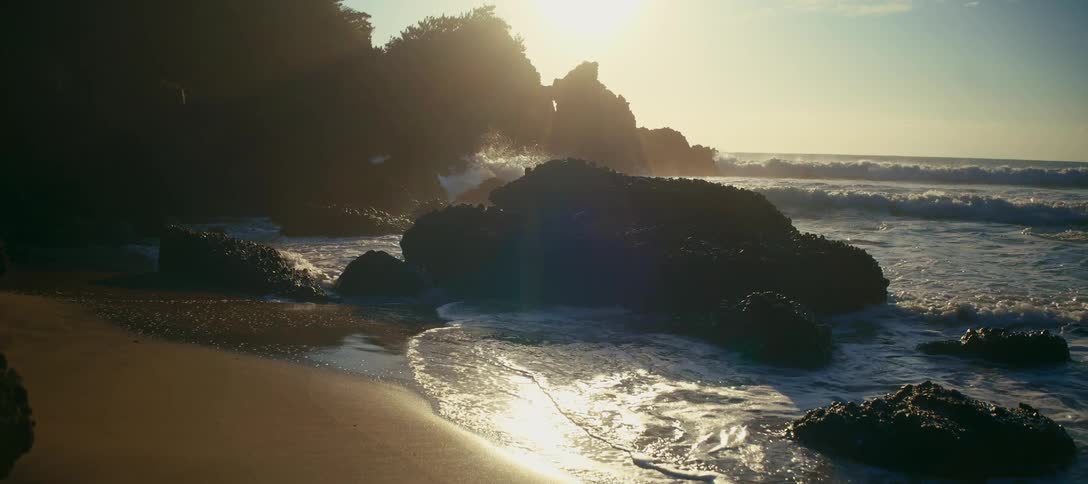 Slow-motion waves crash on a rocky shoreline during a beautiful golden sunrise