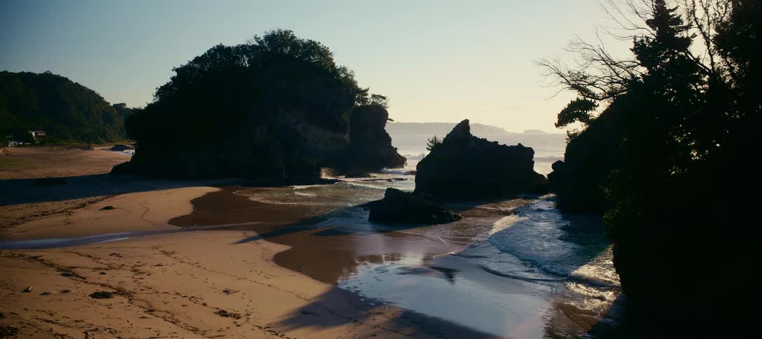 A serene view of a secluded beach cove with rocky islands silhouetted by the warm light of sunrise