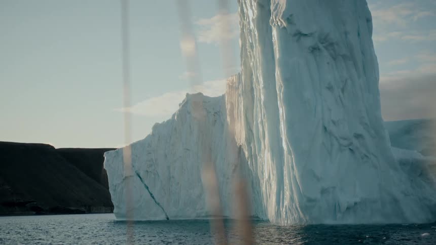A majestic iceberg floats in the calm arctic ocean as the golden sun reflects on the water's surface