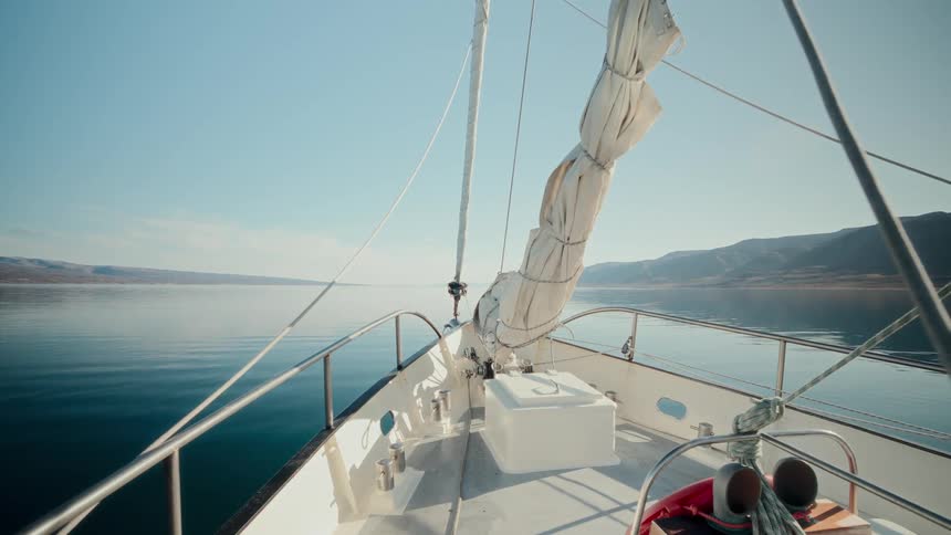 Point of view from the bow of a sailboat gliding across a tranquil lake on a beautiful, sunny day