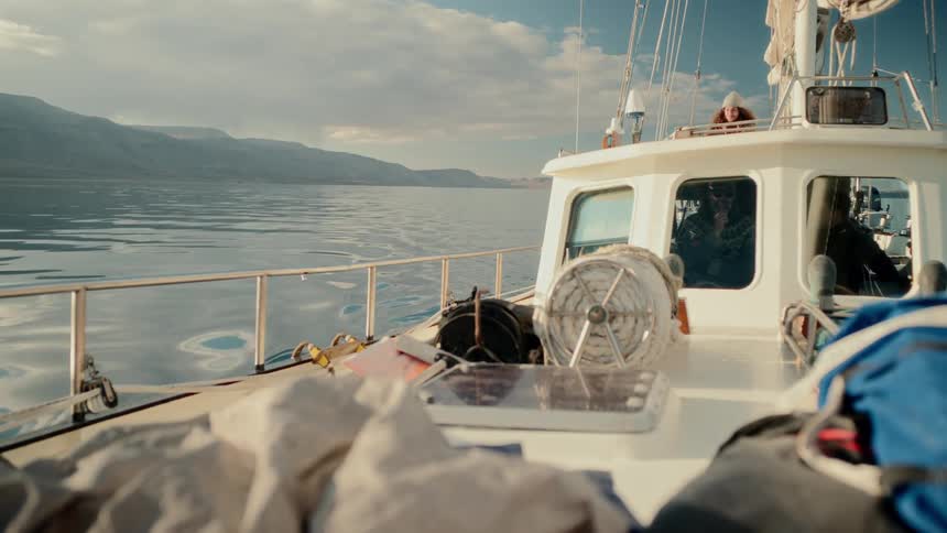 Travelers relax on a sailboat cruising through the serene waters of a massive fjord surrounded by majestic mountains