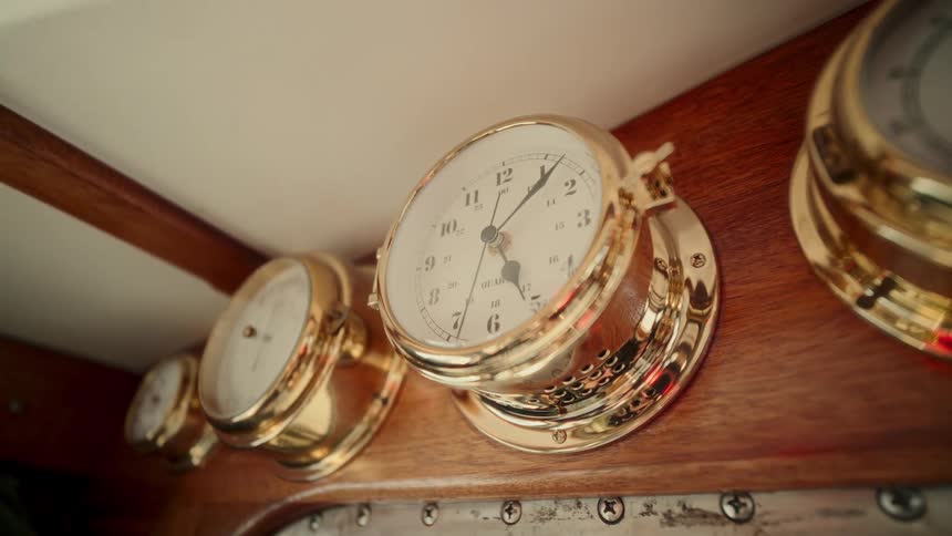 A classic brass nautical clock ticks away the seconds inside the warm, wooden cabin of a ship