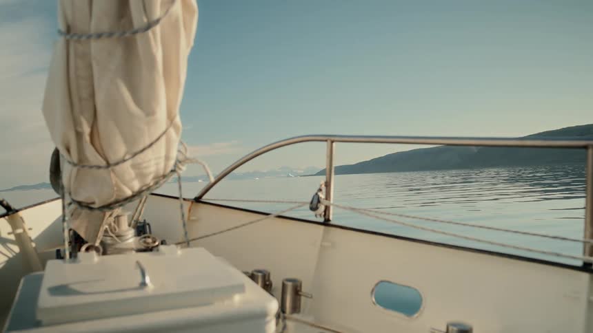 A sailboat glides through the serene, glassy waters of an arctic fjord, with majestic snow-capped mountains in the distance
