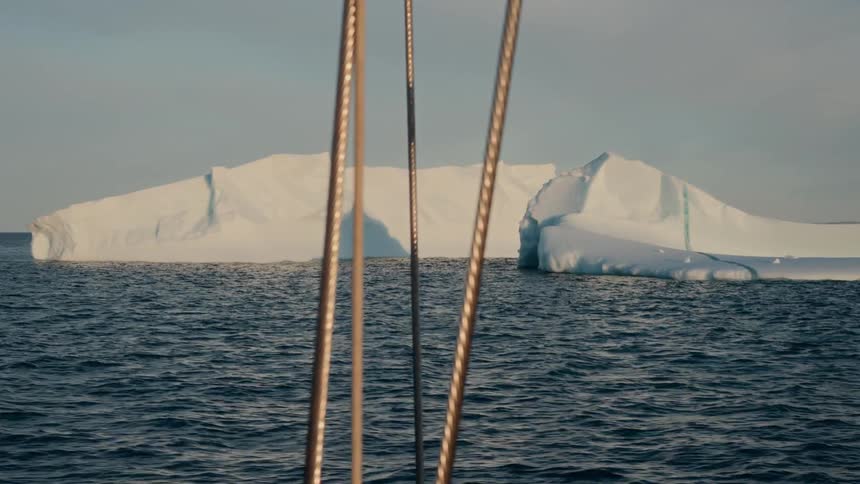 Sailing through a tranquil sea, a massive iceberg looms on the horizon under a clear sky