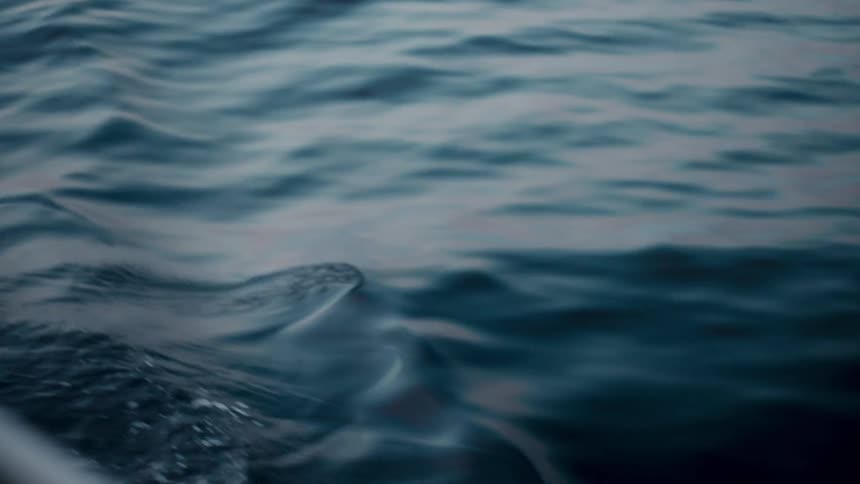 A close-up, slow-motion view captures the hypnotic movement of a boat's wake on the deep blue sea