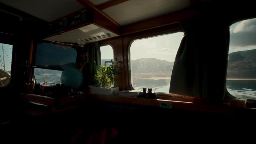 A slow zoom-out from inside a cozy wooden boat cabin reveals a tranquil mountain fjord view through the window