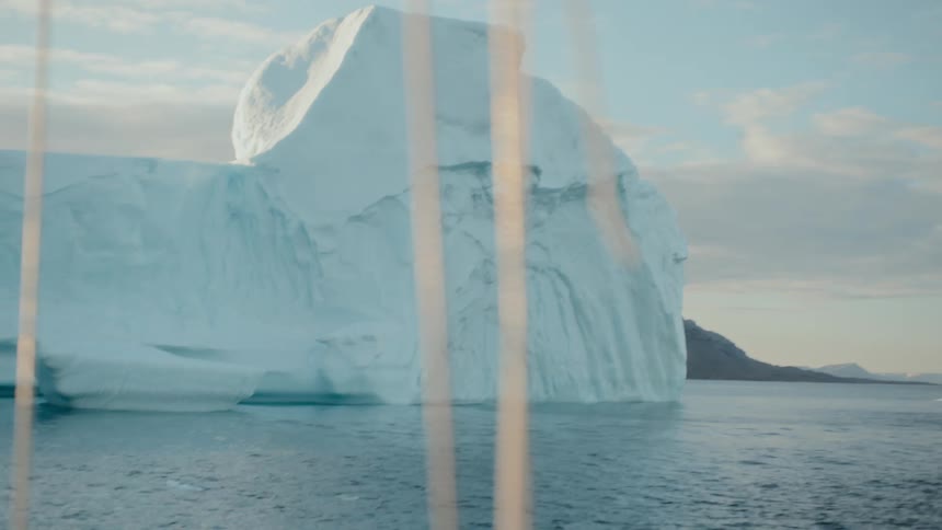 A stunning tilt shot from a boat reveals a colossal iceberg floating in the serene arctic ocean