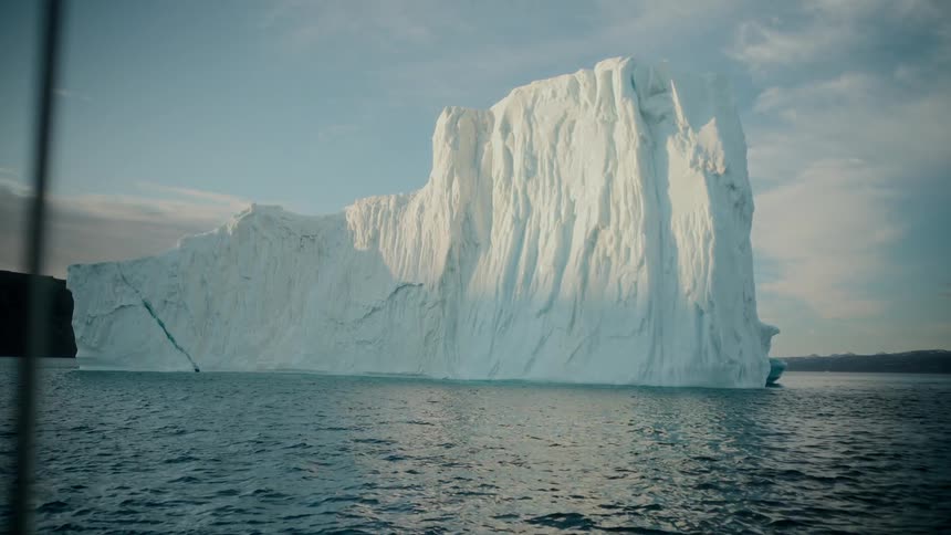 An awe-inspiring view from a boat as it sails by a massive, sunlit iceberg floating in the ocean