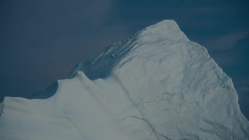 A majestic close-up shot of a towering iceberg peak against a moody blue sky