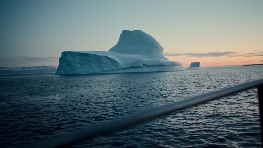 A serene view from a boat sailing past a massive iceberg in the arctic ocean at dusk