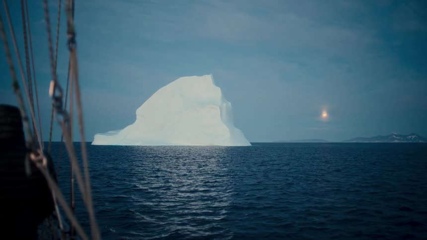 A majestic iceberg looms in the distance as a sailboat glides through the calm Arctic sea under a bright, glowing moon