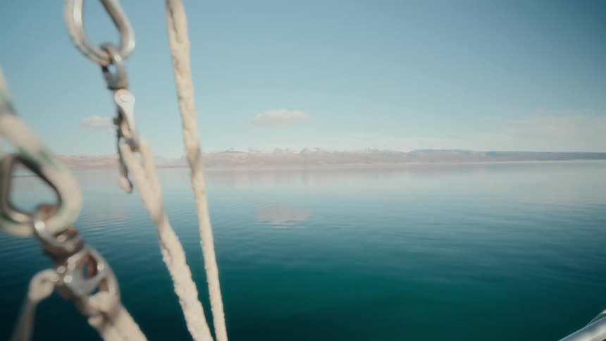A tranquil view from a boat showing a slow rack focus from the calm, glassy lake and distant mountains to the ropes and rigging