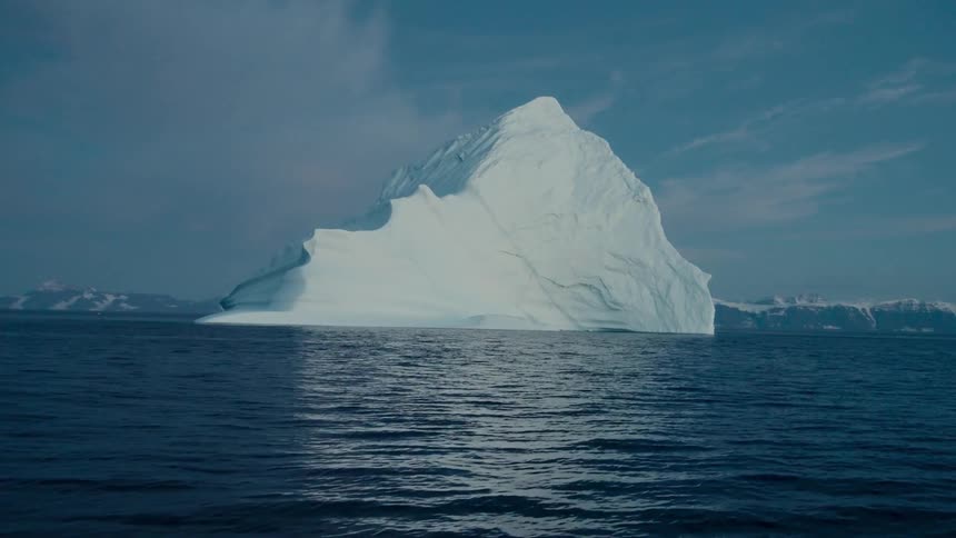 A majestic iceberg floats serenely in the deep blue Arctic ocean with snowy mountains in the distance