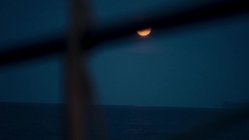 Timelapse of a golden moon rising over the calm ocean at twilight, viewed from a boat