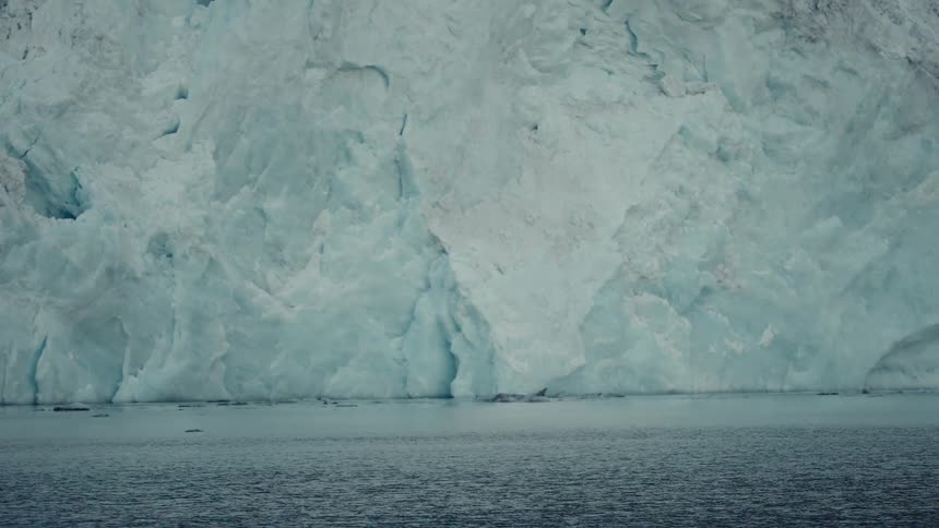 A majestic, static view of a massive glacier wall meeting the calm arctic water