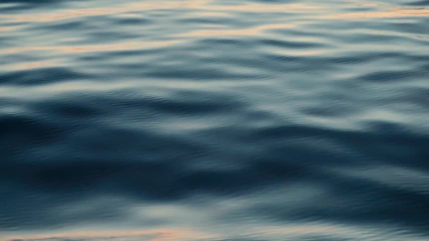 A serene close-up of gentle dark blue water ripples reflecting the soft light of dusk