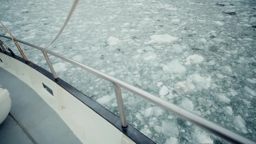 A boat sits moored in a calm sea filled with drifting chunks of ice