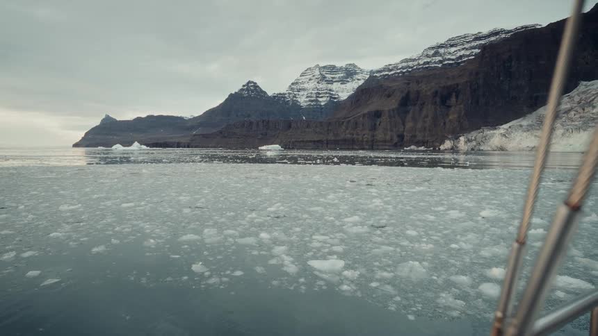 A steady shot from a boat sailing through the tranquil but frigid waters of an arctic fjord with glaciers and mountains in view