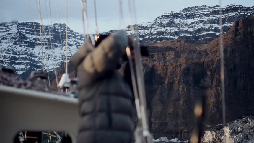 A photographer on a sailboat captures the majestic snow-capped mountains of a vast arctic landscape