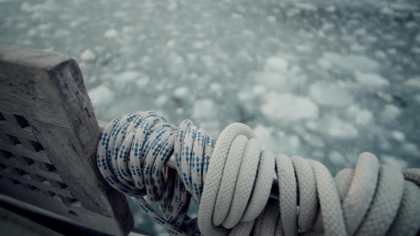 A focus pull from a sea filled with chunks of floating ice to a rope coiled on the side of a boat