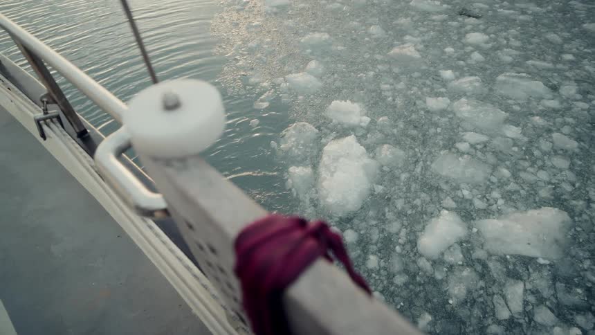 Close up from the side of a boat as it sits in calm, icy water