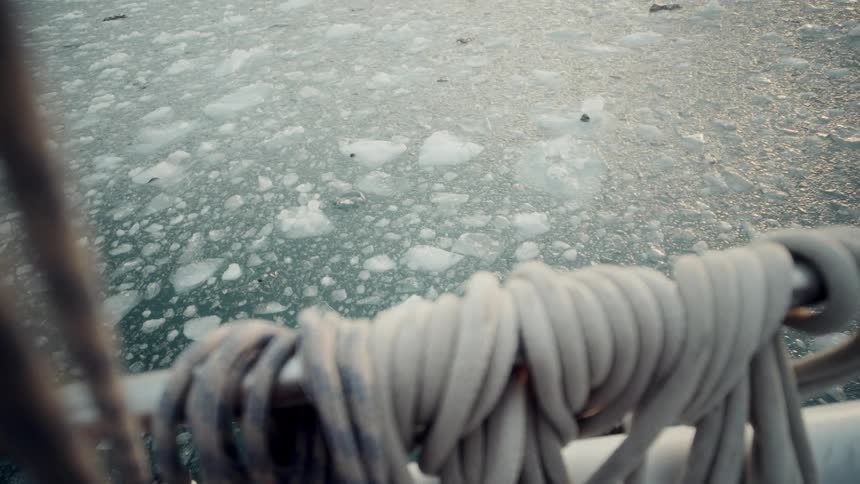 View from a boat's deck with coiled ropes looking down onto a sea filled with floating ice slush