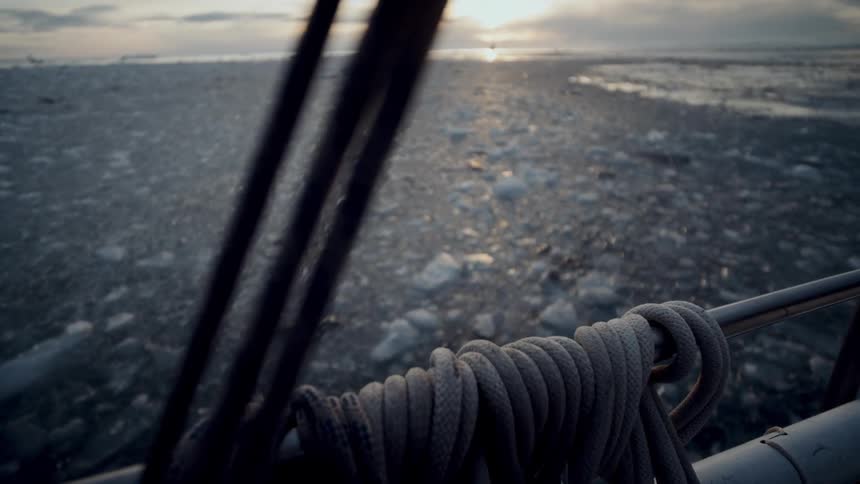 Rack focus from a sunset over a frozen arctic sea to a coiled rope on the railing of a ship