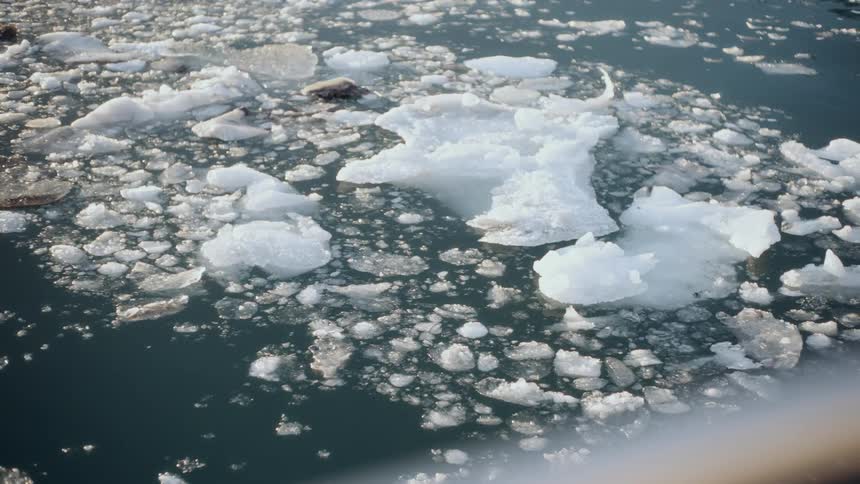 A close-up view from a boat shows chunks of melting ice floating and drifting in the cold, dark ocean water