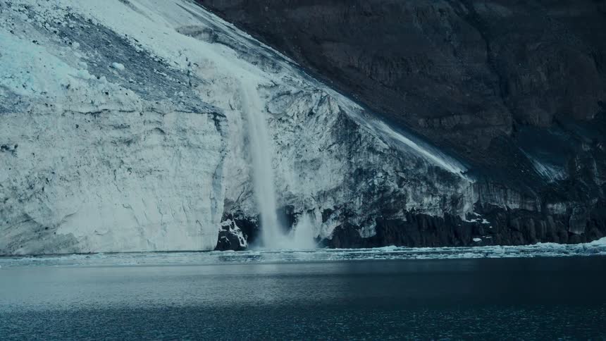 A powerful avalanche of snow and ice cascades down from a massive glacier into the dark, cold water below
