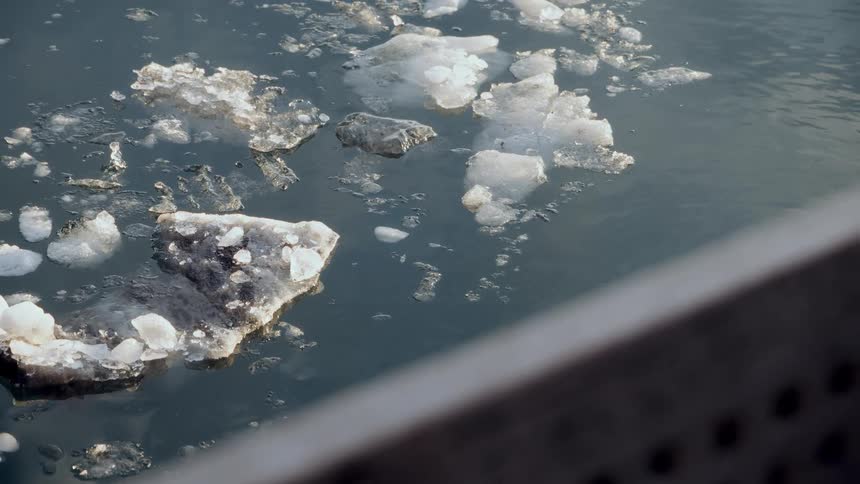 A close-up view shows slushy pieces of ice gently floating in the dark water as they slowly melt
