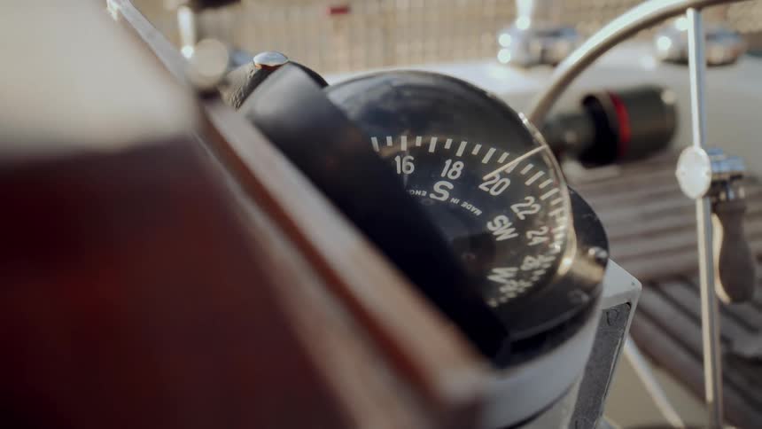 A detailed close-up shot of a sailboat's compass mounted on the wooden helm