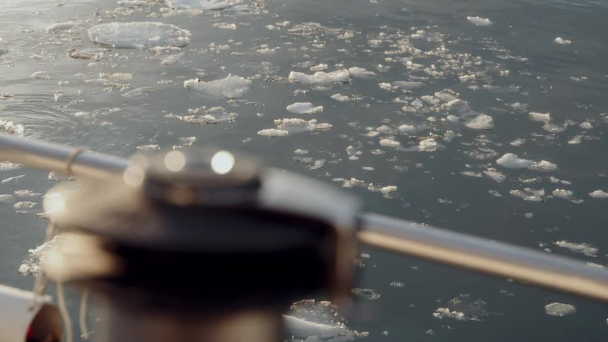 A serene, high-angle view from a boat captures chunks of ice and slush floating in the tranquil arctic water