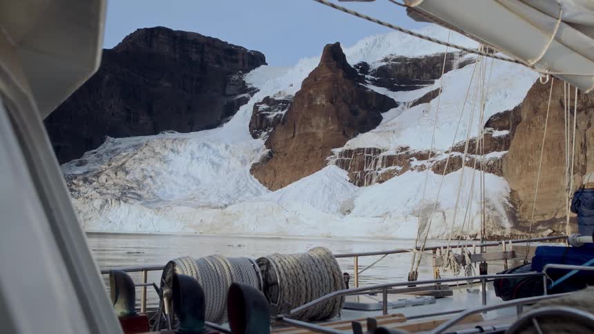A stunning view of a massive glacier and snow-covered mountains from the deck of a ship in an icy fjord