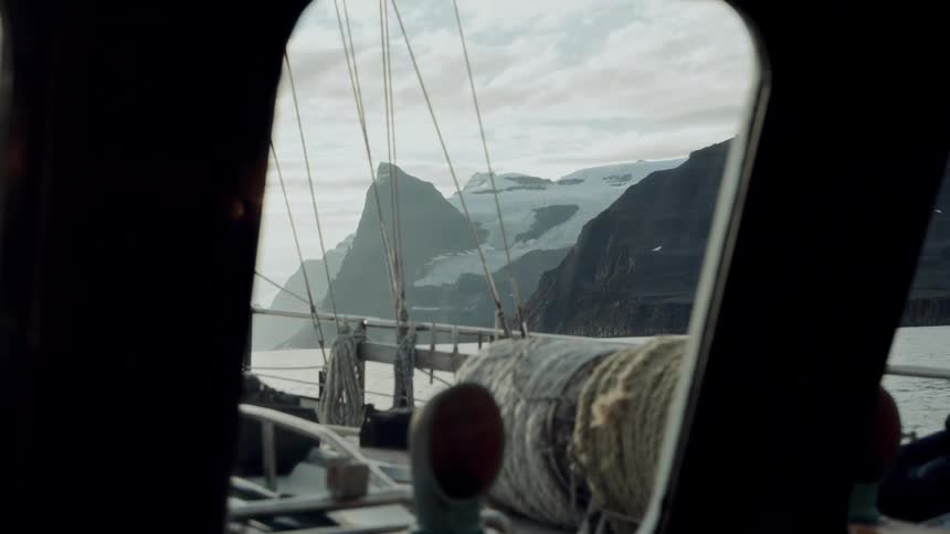A majestic glacier and rugged mountains are seen from the window of a boat sailing through a tranquil fjord