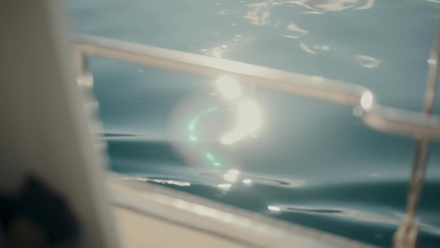 A serene, abstract view of sunlight glistening and reflecting off the calm blue sea from the side of a boat