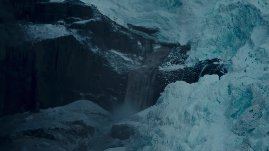 A powerful waterfall of meltwater cascades down a massive, icy blue glacier in a cold, remote landscape