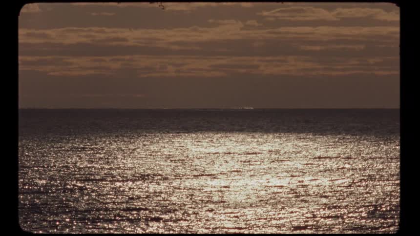 Sunlight glitters across the ocean horizon under a cloudy sky in a peaceful vintage film shot