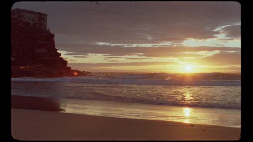 Vintage Super 8mm footage shows a beautiful sunrise reflecting on the ocean waves at a tranquil beach