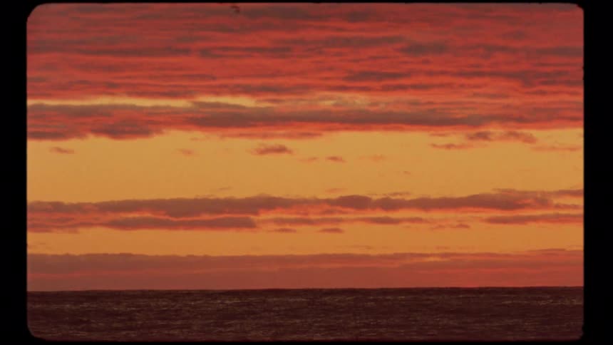 A vintage 8mm style clip shows a vibrant red and orange sunset over the calm ocean horizon
