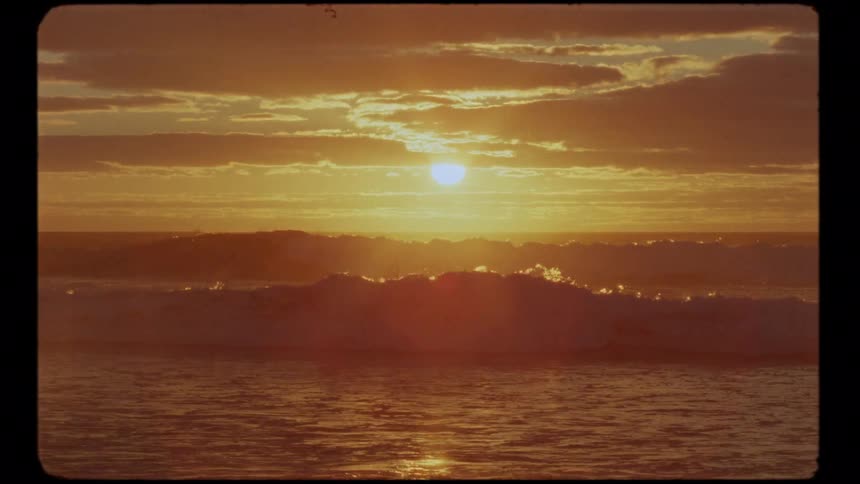 A vintage film captures the golden sun setting over rolling ocean waves