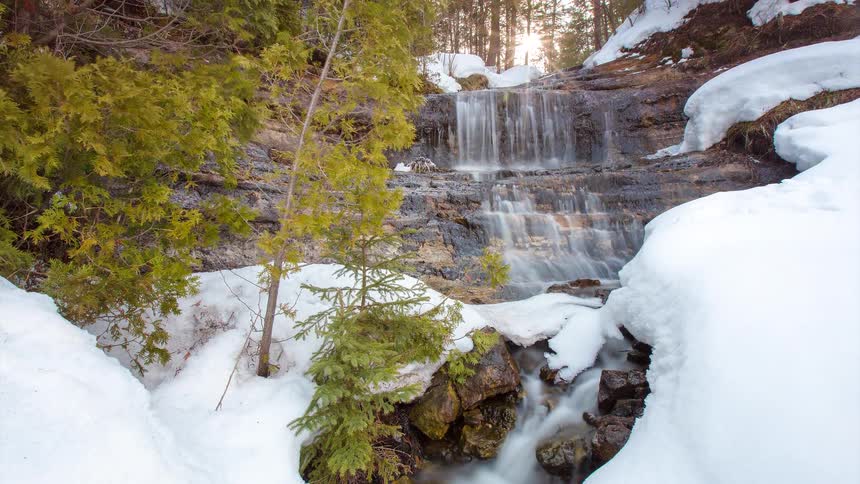 Beautiful time-lapse of a snowy waterfall in a winter forest as the sun sets
