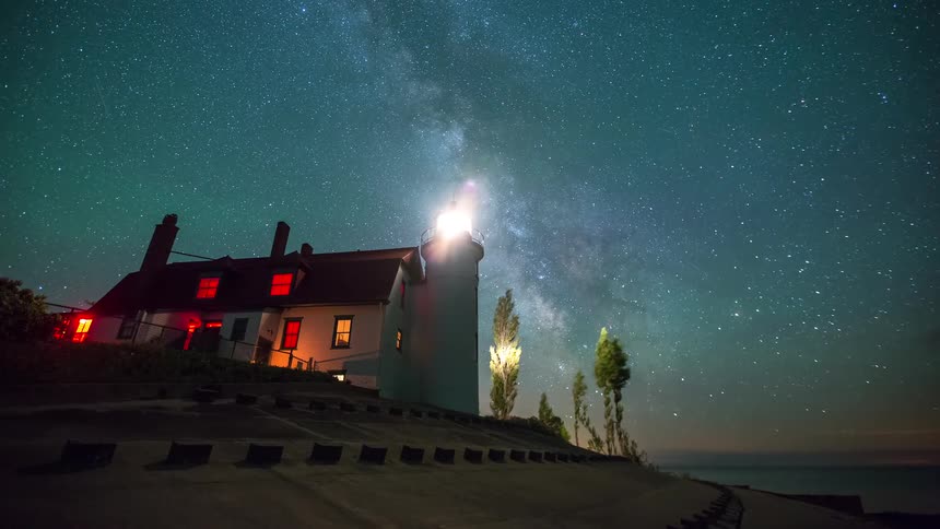 A stunning timelapse shows the Milky Way galaxy moving across a star-filled night sky above a glowing lighthouse on the coast