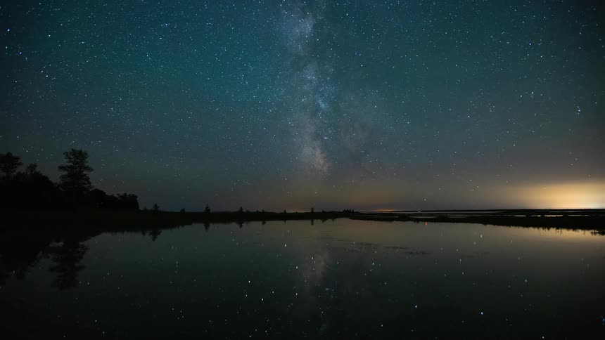 A stunning time-lapse captures the Milky Way galaxy and stars rotating in the night sky, their light reflecting perfectly in a still body of water
