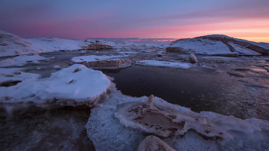 A beautiful time-lapse of a vibrant sunrise over a vast, frozen winter landscape covered in ice and snow