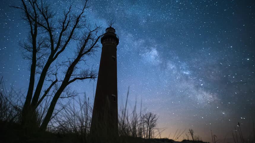 A stunning timelapse captures the Milky Way galaxy arcing across the star-filled night sky behind a historic lighthouse